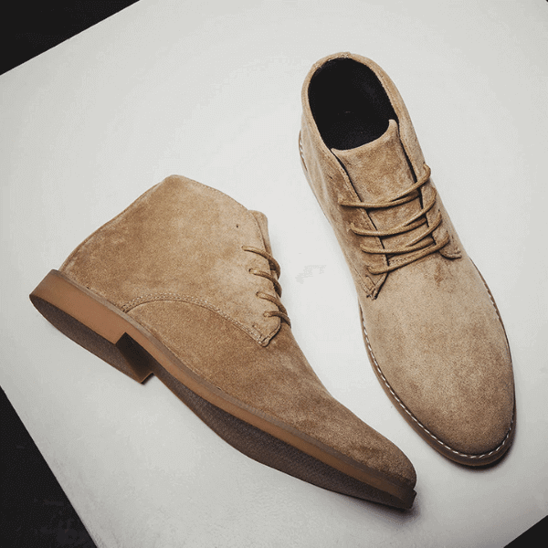 Pair of tan suede luxury men's boots in Chukka style with lace-up design on neutral background
