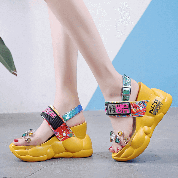 Chunky yellow luxury women's sandals with colorful straps and decorative gems on a model's feet