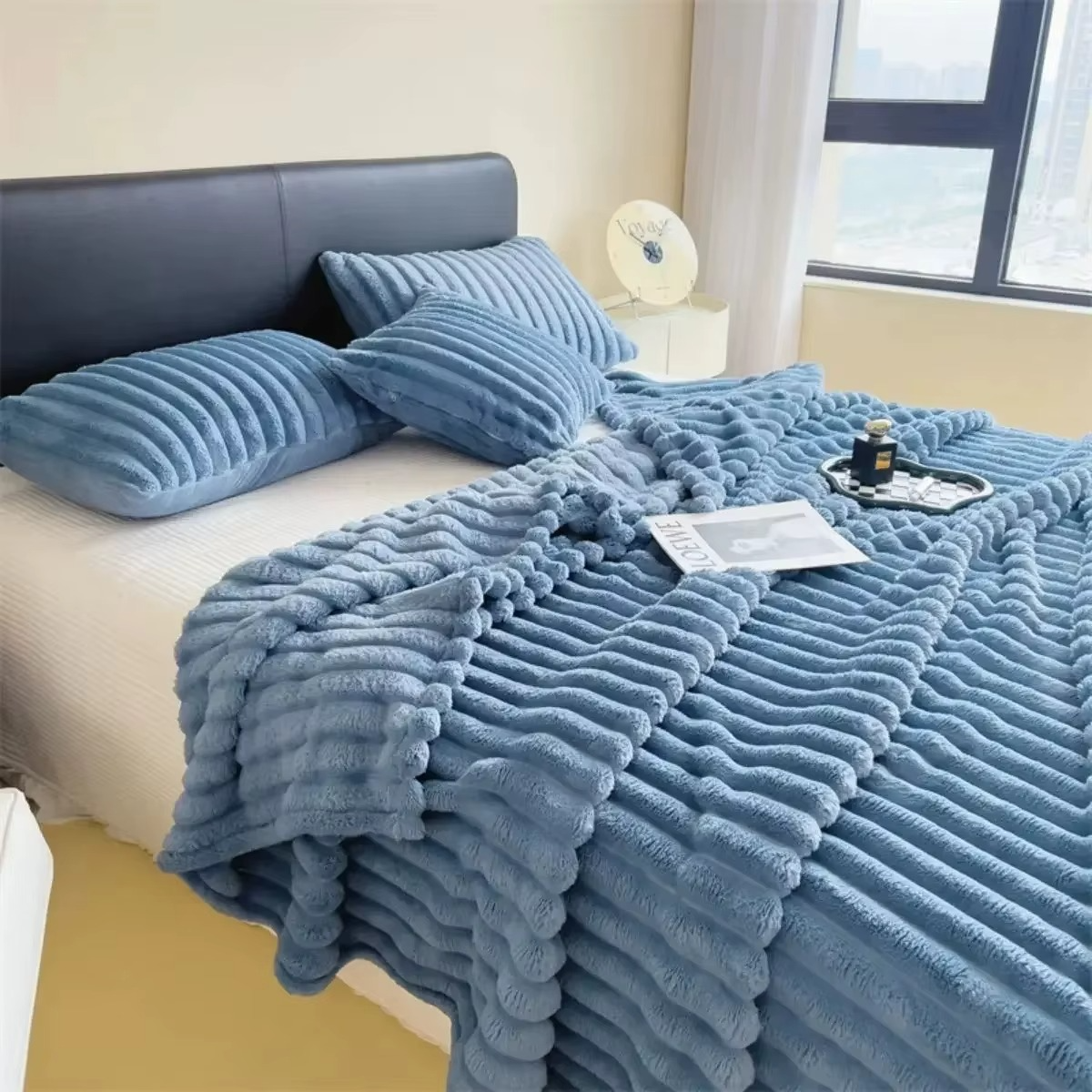 Soft plush velvet blanket in blue draped over a bed with pillows and decorative items
